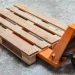Wooden pallet on an orange pallet jack ready to move on a concrete warehouse floor.【informative】